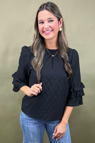 Woman wearing a black blouse with ruffled sleeves against a beige background