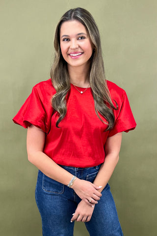 Woman wearing a red shirt and blue jeans against a green background