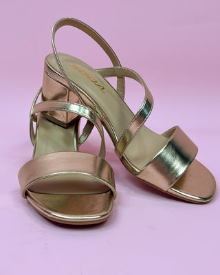Gold high-heeled sandals on a pink background