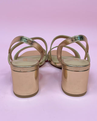 Gold high-heeled sandals on a pink background
