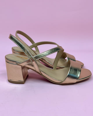 Gold high-heeled sandals on a pink background