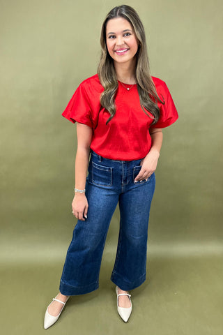 Woman wearing a red blouse and blue jeans against a green background