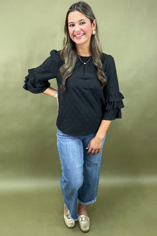 Woman wearing a black blouse with ruffled sleeves and blue jeans on a green background
