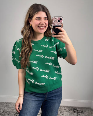Person wearing a green shirt with white text, taking a mirror selfie.