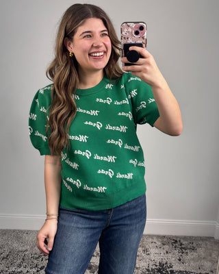 Person wearing a green t-shirt with white text pattern, taking a selfie.