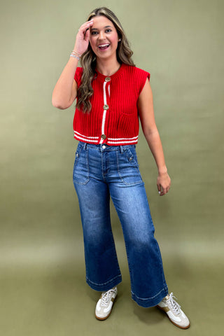 Woman wearing a red top with white trim and blue jeans on a green background