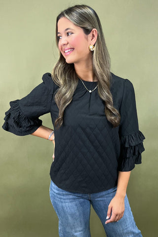 Woman wearing a black blouse with ruffled sleeves against a green background