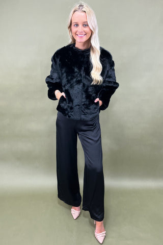 Woman wearing a black fluffy sweater and black pants on a green background
