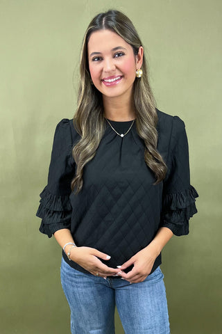 Woman wearing a black blouse with ruffled sleeves against a green background