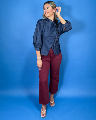 Dark wash denim tie-front top featuring a structured stand collar, puff three-quarter sleeves, asymmetrical front, and statement bow-tie closures.