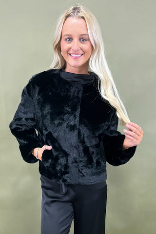 Woman wearing a black faux fur jacket against a plain background