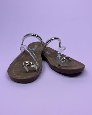 Pair of sandals with metallic straps on a light purple background