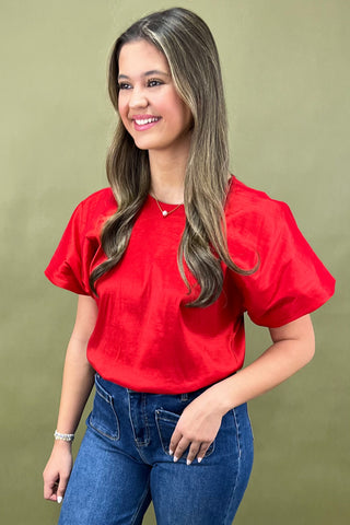 Woman wearing a red blouse and blue jeans against a green background