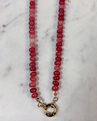 A beaded necklace made of round faceted beads in shades of pink and red,