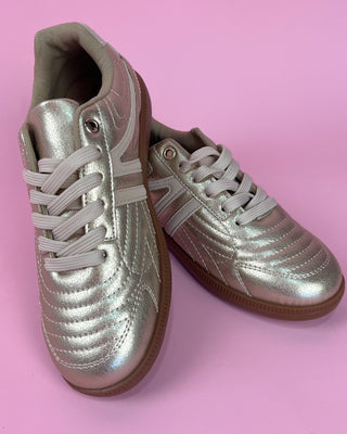 Gold metallic lace-up sneaker with white accents and gum sole on pink background