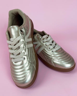 Gold metallic lace-up sneaker with white accents and gum sole on pink background