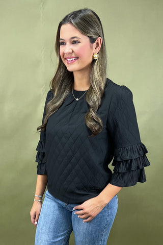 Woman wearing a black blouse with ruffled sleeves against a green background