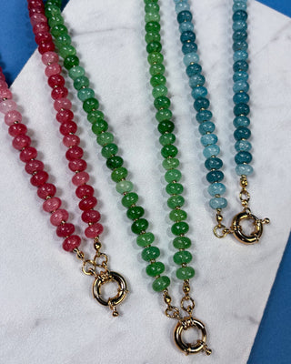 Three beaded gemstone necklaces arranged vertically on a white marble surface