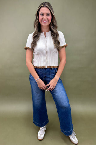 Woman wearing a white blouse with brown trim and blue jeans against a green background