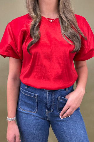 Person wearing a red t-shirt and blue jeans against a beige background