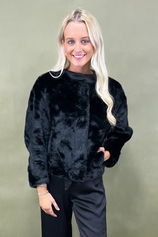 Woman wearing a black fur jacket against a plain background