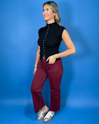 Black ribbed knit sleeveless top featuring a mock neckline, contrasting button-front detail, fitted silhouette, and pointed split hem.