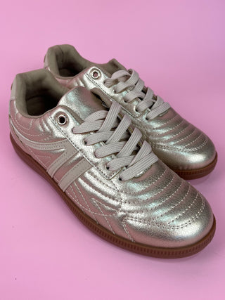 Gold metallic lace-up sneaker with white accents and gum sole on pink background