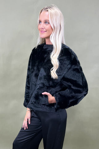 Woman wearing a black fluffy sweater against a plain background