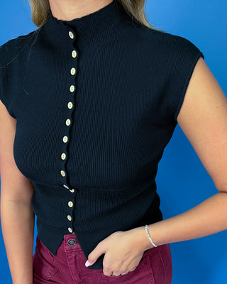 Black ribbed knit sleeveless top featuring a mock neckline, contrasting button-front detail, fitted silhouette, and pointed split hem.