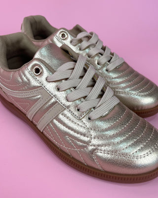 Gold metallic lace-up sneaker with white accents and gum sole on pink background
