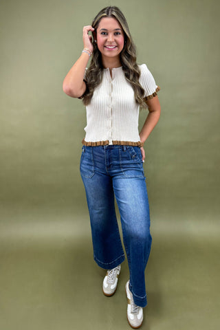 Woman wearing a white blouse with ruffled sleeves and blue jeans on a green background
