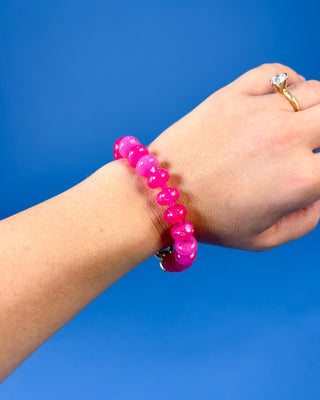 A bright pink beaded bracelet worn on a person's wrist