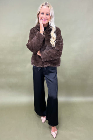 Woman wearing a brown faux fur jacket and black pants on a green background