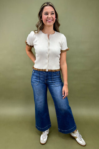 Woman wearing a white blouse with brown trim and blue jeans against a green background
