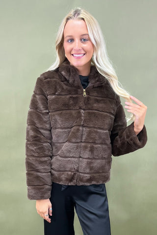 Woman wearing a brown faux fur jacket against a green background