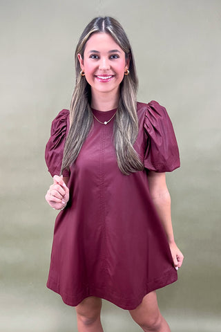 Woman wearing a burgundy dress with puff sleeves against a beige background