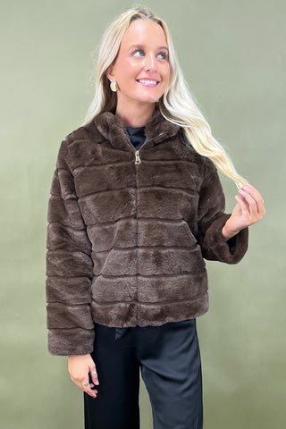 Woman wearing a brown faux fur jacket against a green background