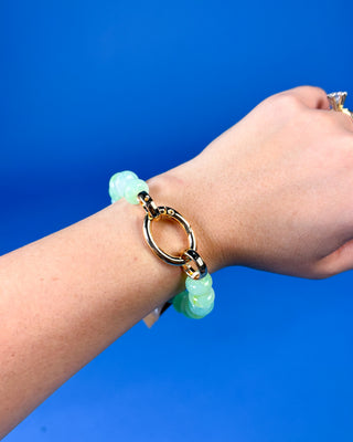 A gold-tone link bracelet with light green jade-like beads worn on a person's wrist