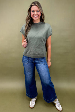 Woman wearing a green sweater and blue jeans against a green background