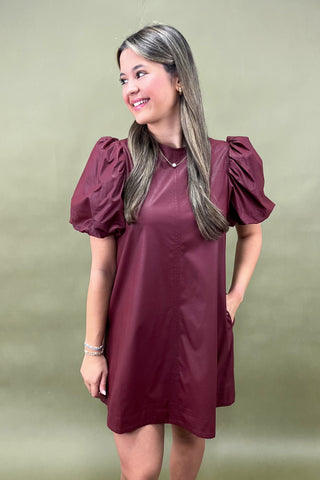 Woman wearing a burgundy dress with puff sleeves against a green background