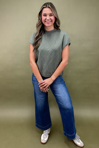 Woman wearing a green textured top and blue jeans against a green background