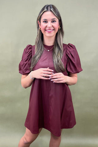 Woman wearing a burgundy dress with puffed sleeves against a green background