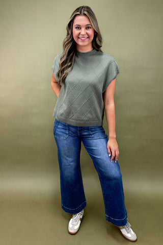 Woman wearing a green top and blue jeans against a green background