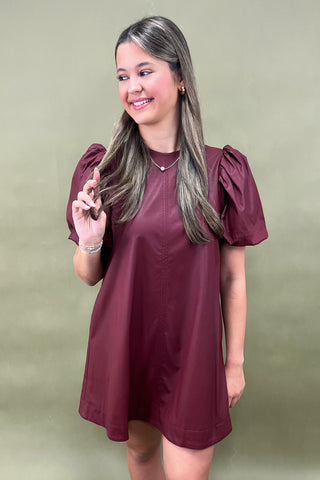Woman wearing a maroon dress with puff sleeves against a green background
