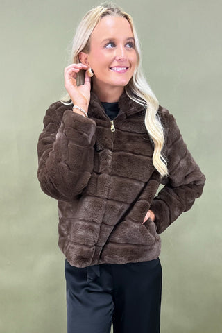 Woman wearing a brown faux fur jacket against a green background
