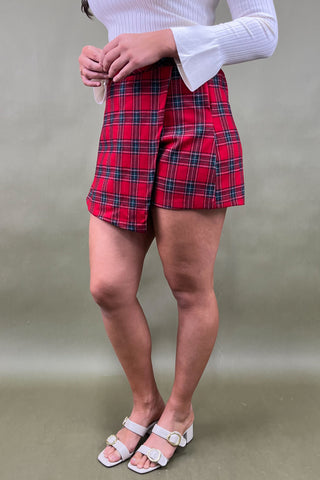 Person wearing red plaid shorts and a white sweater on a plain background