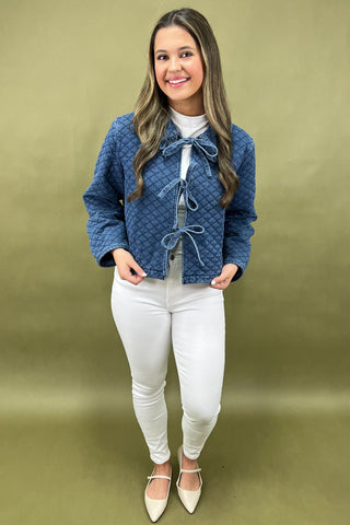 Woman wearing a blue quilted jacket and white pants against a green background