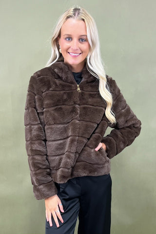 Woman wearing a brown faux fur jacket against a green background