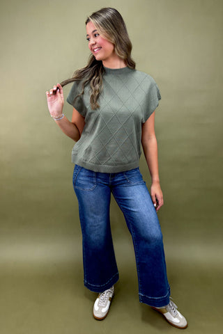 Woman wearing a green top and blue jeans against a beige background