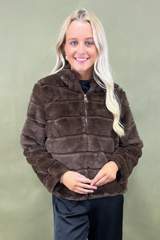 Woman wearing a brown faux fur jacket against a green background